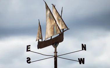 Metal weather vane shaped like a sailing ship with compass directions, symbolizing data-driven navigation, AI-guided decision making, and strategic direction in digital transformation