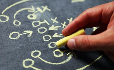 Hand draws American football gameplay strategy on blackboard in chalk