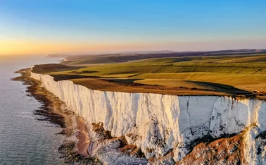 Aerial view of white cliffs and green downland. The sky is blue and the sun is setting