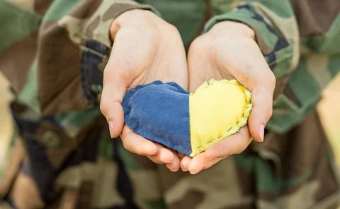 Close-up of a military person’s hands holding a heart-shaped Ukraine flag
