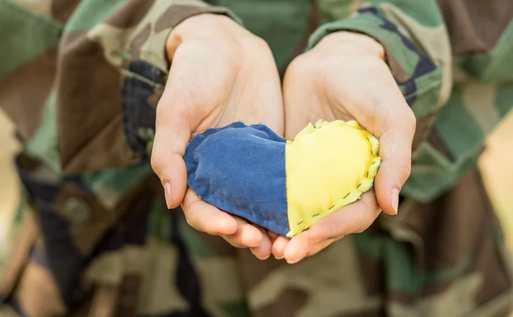 Close-up of a military person’s hands holding a heart-shaped Ukraine flag