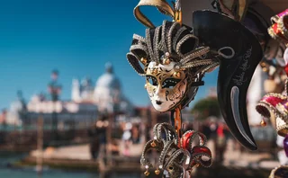 Colorful Venetian mask hanging by the waterfront during a sunny day