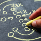 Hand draws American football gameplay strategy on blackboard in chalk