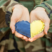 Close-up of a military person’s hands holding a heart-shaped Ukraine flag